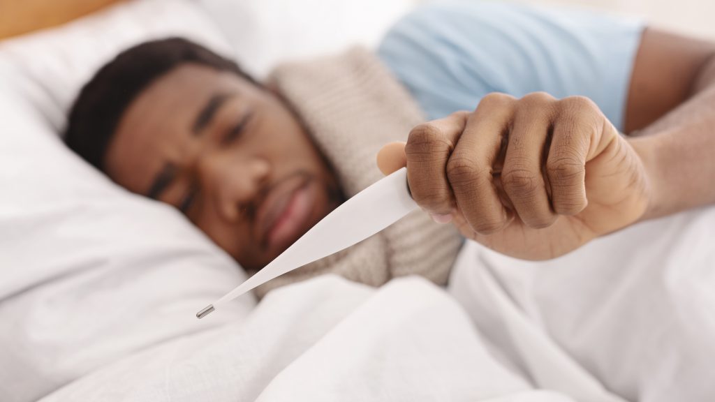 Man lying in bed sick holding a thermometer to check his temperature.