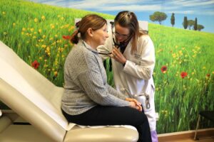 Women's Health Provider giving a check-up to a female patient sitting on an exam chair in a room decorated to look like a grassy field.