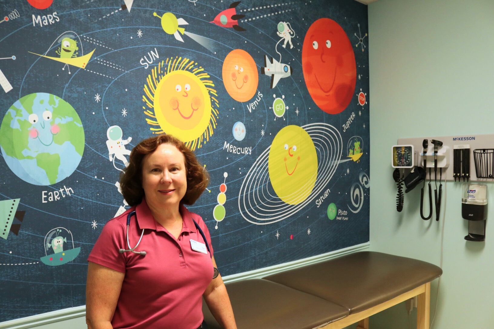 Pediatrics provider Mary Dressler-Carre posing for a photo in an exam room decorated like the solar system.