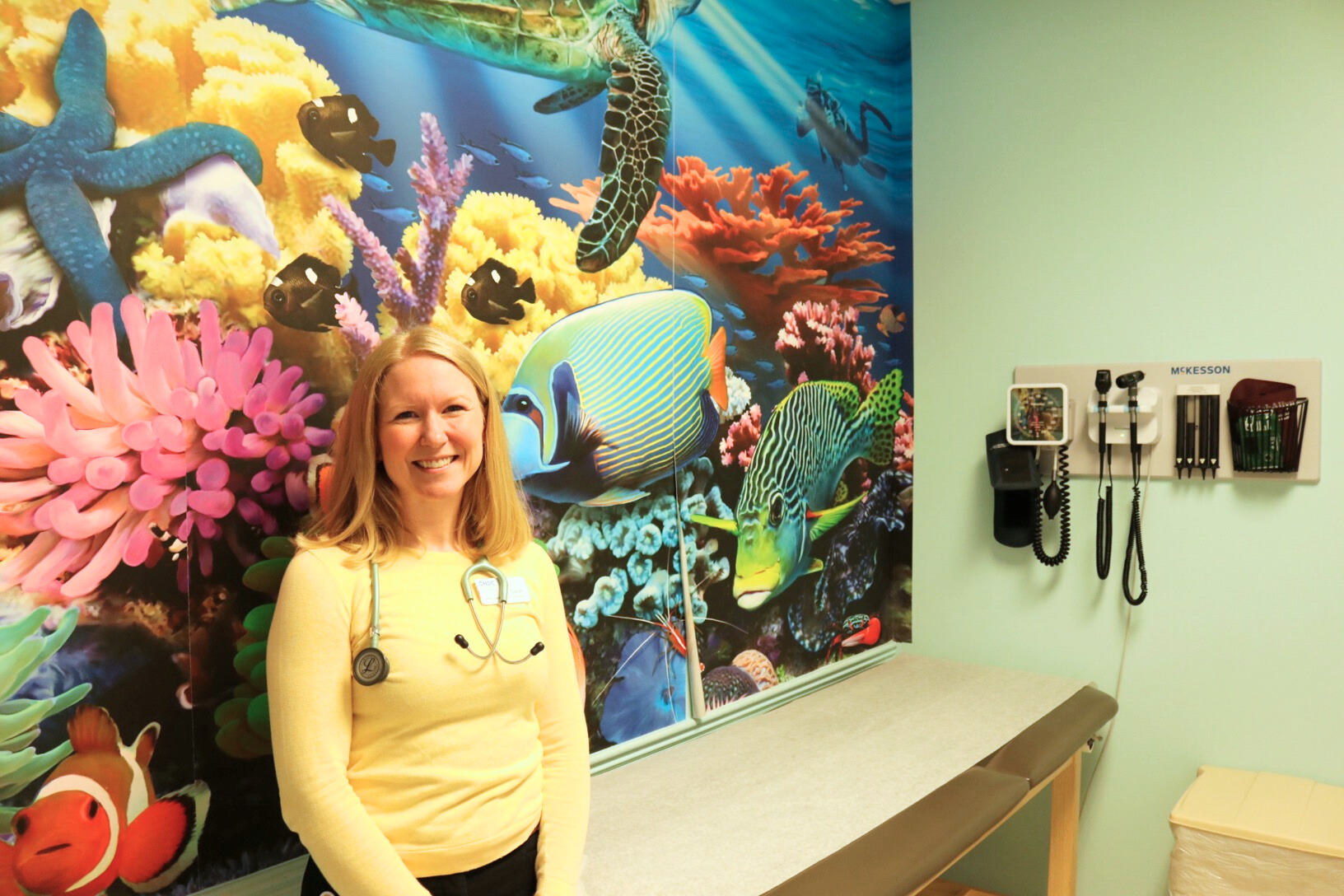 Pediatrics doctor Sarah Spengler posing for the camera in an exam room decorated like the ocean.