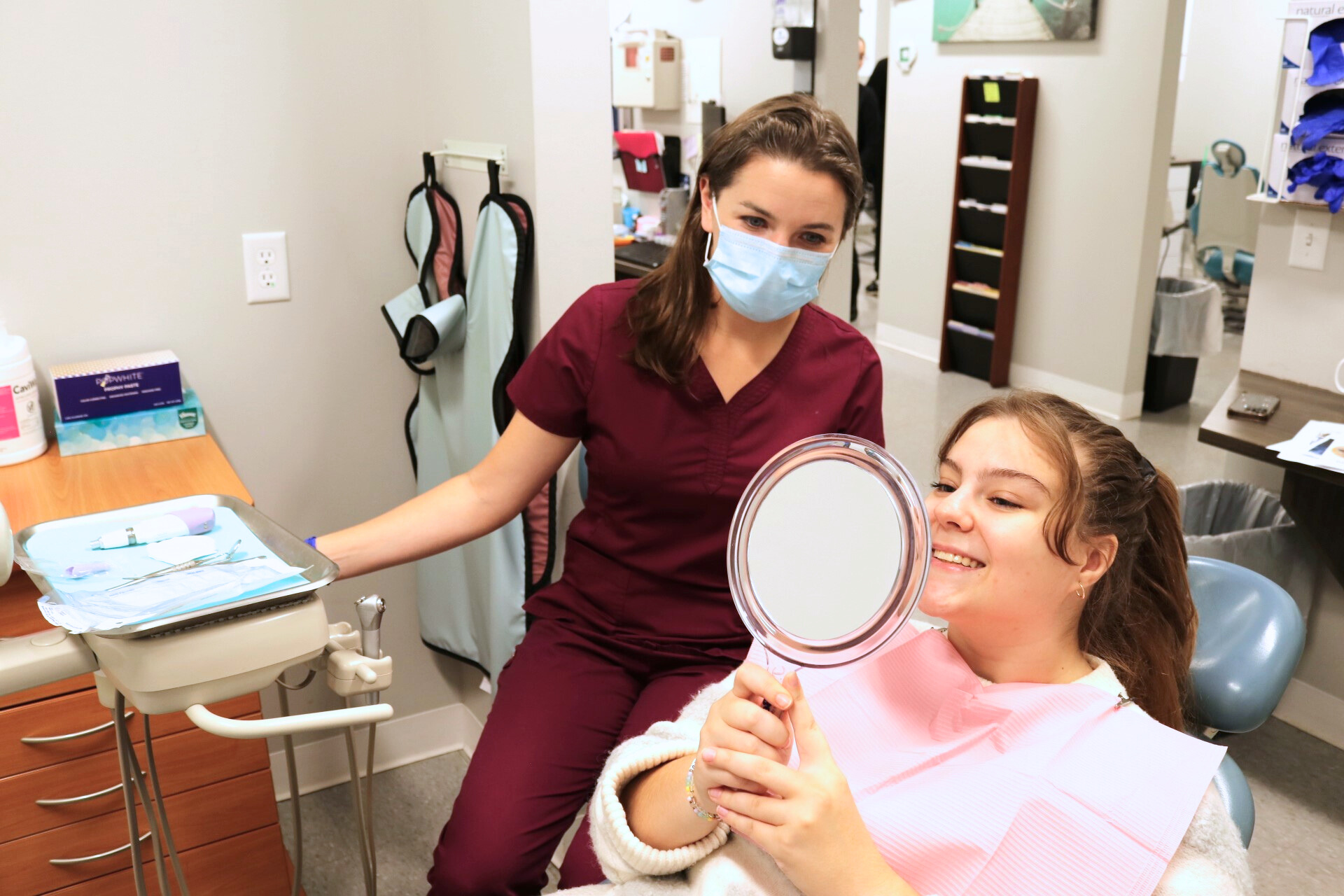 Patient looking at her teeth through a mirror approve of the dental work done by the dentist.