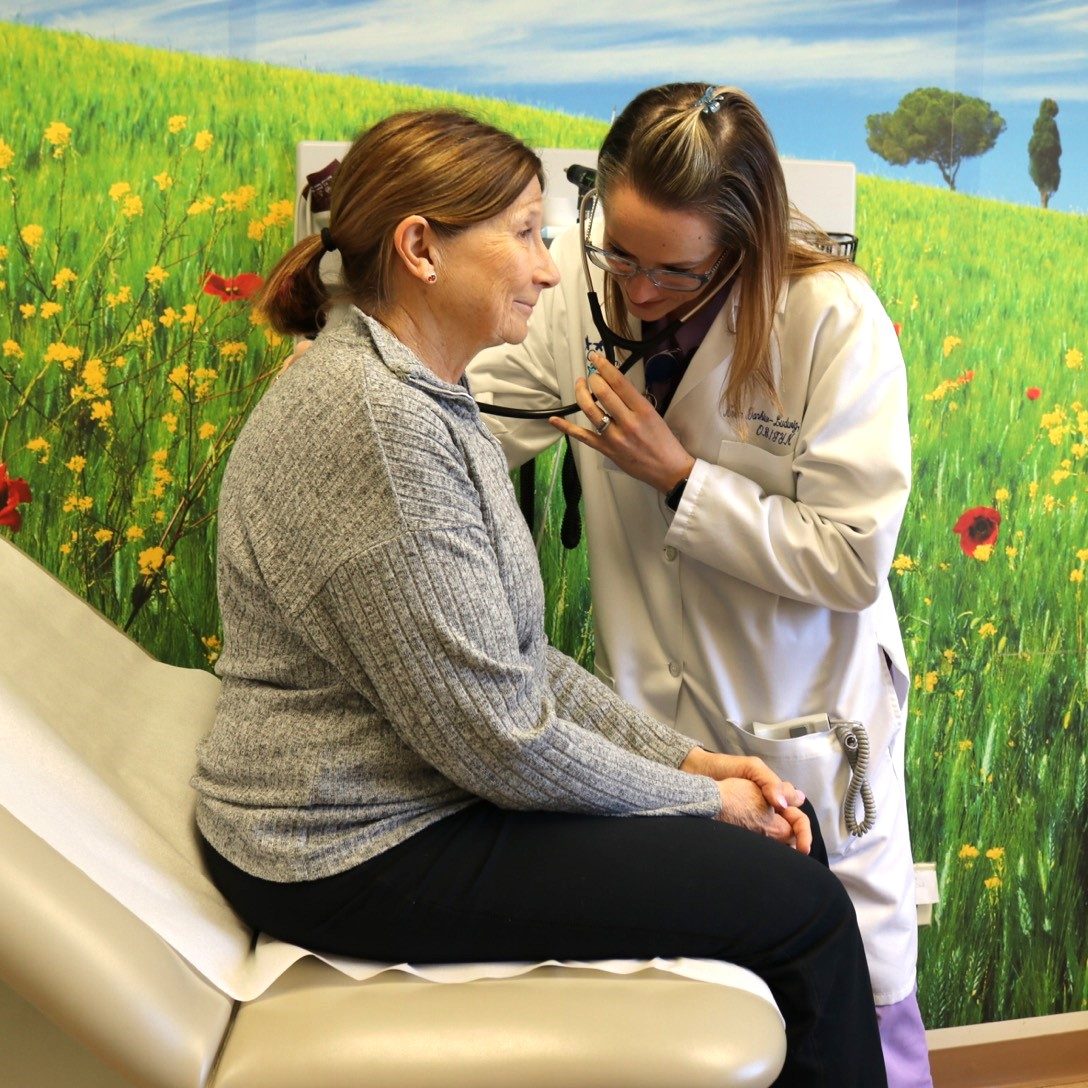 Women's Health Provider giving a check-up to a female patient sitting on an exam chair in a room decorated to look like a grassy field.